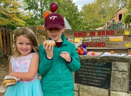 Two children stand in front of a sign for Hand in Hand playground, holding pastries.
